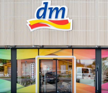 Exteriér obchodu dm s farebnými grafickými prvkami na oknách a výrazným logom nad vchodom.