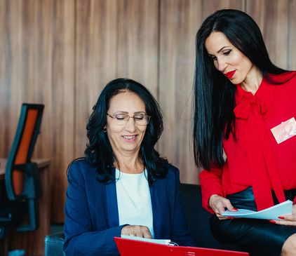 Две колежки, седнали на бюро, преглеждат документи