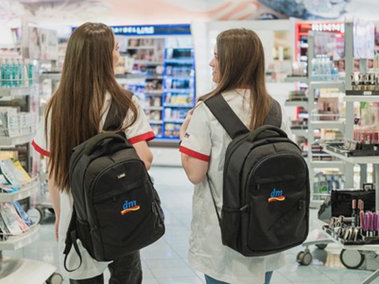 Две момичета, облечени работно облекло и с ученически раници на гърба са в dm магазин.